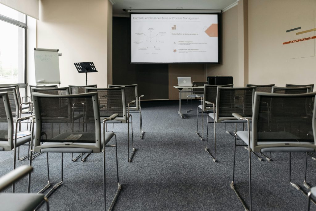 pexels-photo-8761299-8761299 An empty conference room with chairs, a projector screen, and presentation setup.